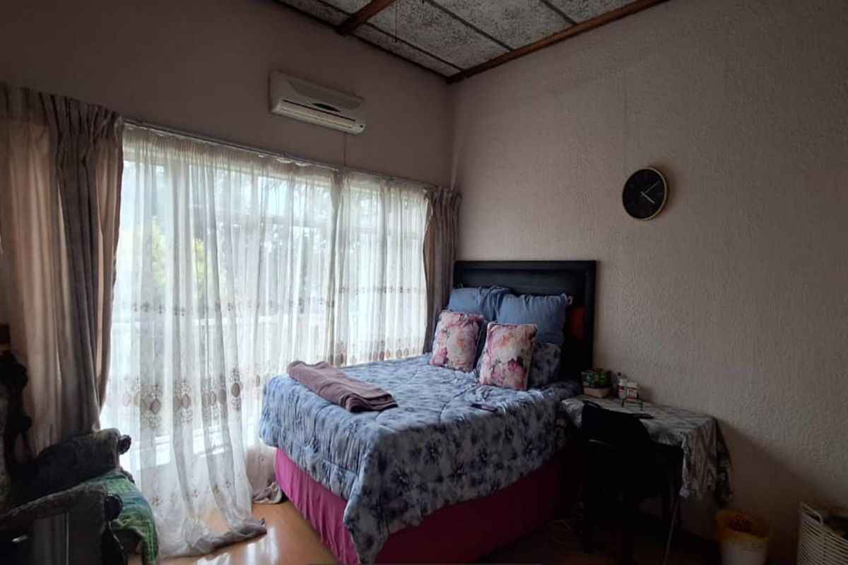 A bedroom featuring a large window with natural light, a wall-mounted air conditioning unit, and textured wall finishes.