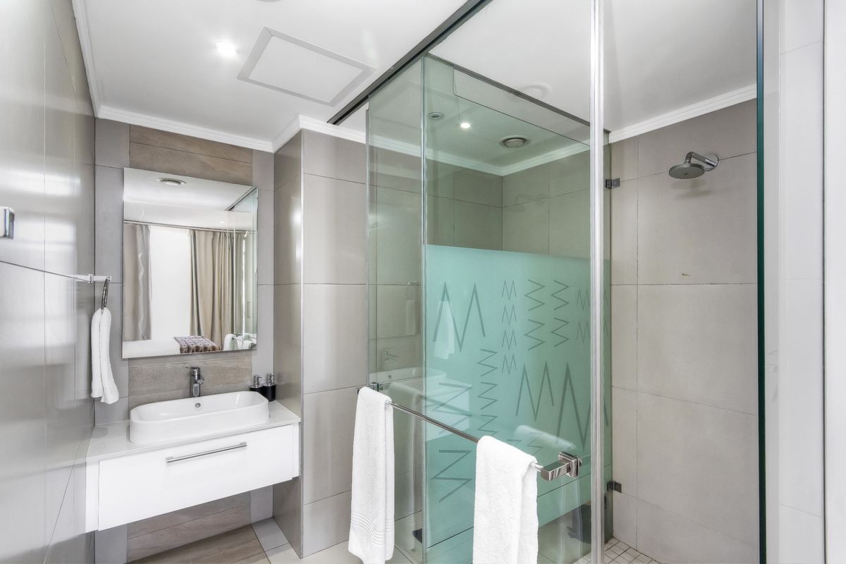 Modern bathroom featuring a wall-mounted vanity with a vessel sink, large mirror, and a spacious glass-enclosed shower with neutral tiling.