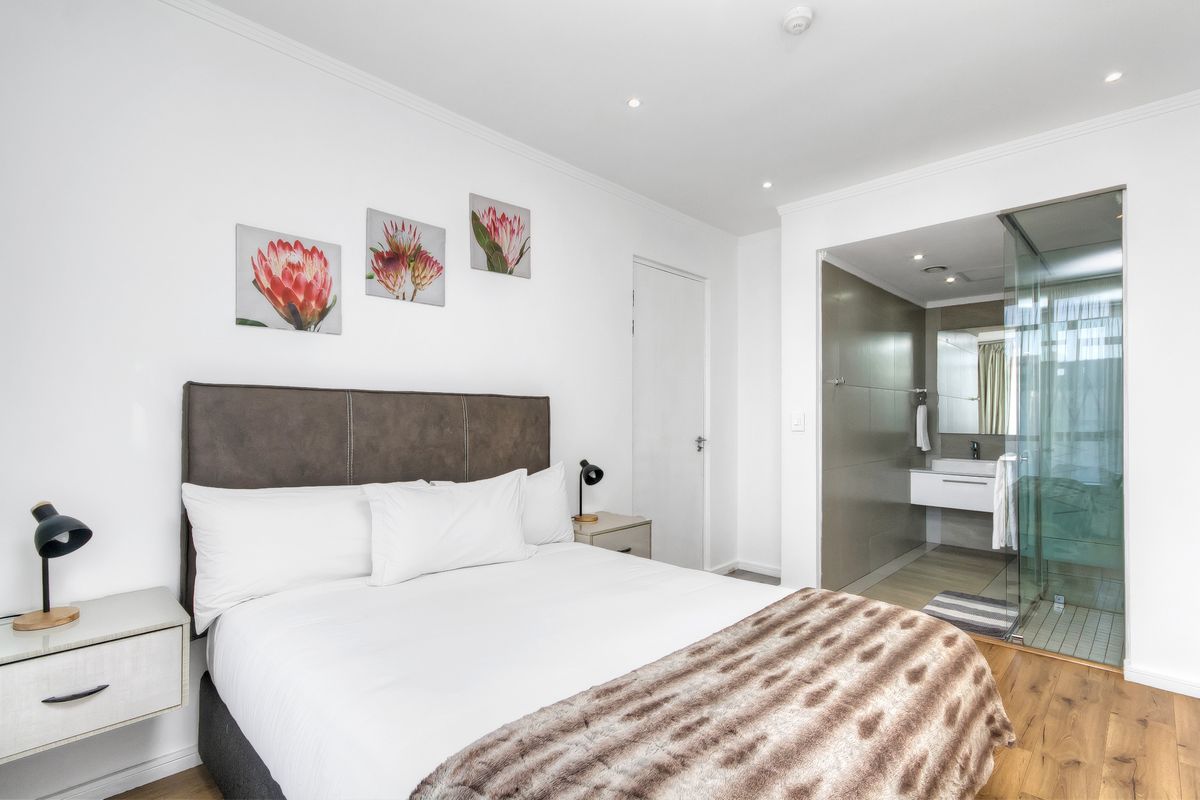 Modern bedroom featuring laminate flooring, recessed lighting, and an open-plan en-suite bathroom with a glass-enclosed shower and contemporary vanity.