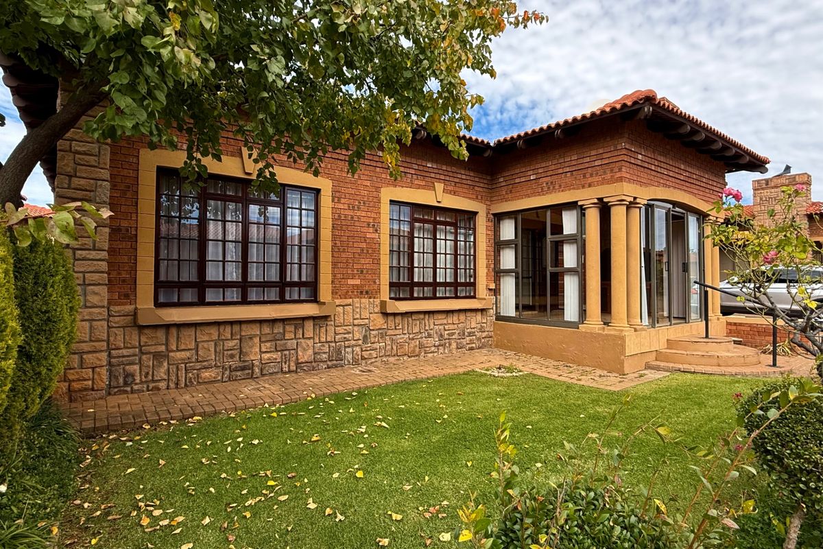 Rear view of a townhouse featuring face brick and stone cladding, a covered patio with columns, and a well-maintained garden area.