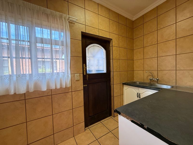 A functional scullery area featuring tiled walls, built-in cabinetry with a stainless steel sink, and direct access to the exterior.