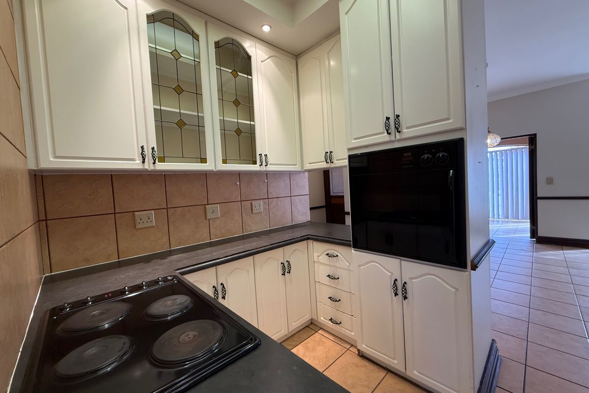 A functional kitchen featuring white cabinetry, built-in oven, electric hob, and tiled backsplash, offering a classic layout with potential for modern updates.