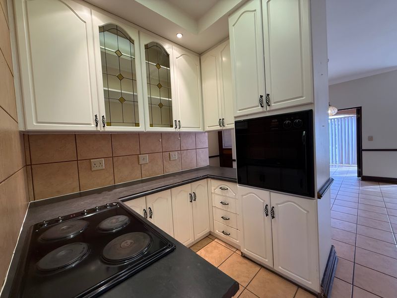 A functional kitchen featuring white cabinetry, built-in oven, electric hob, and tiled backsplash, offering a classic layout with potential for modern updates.