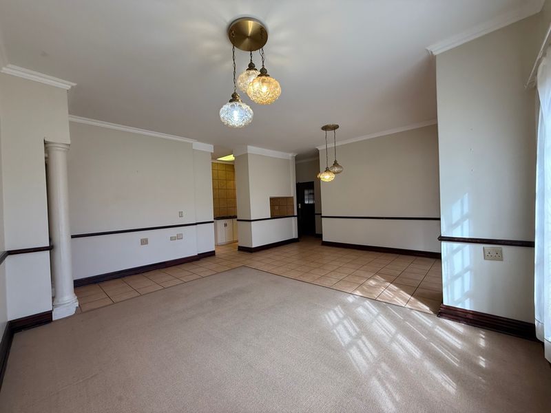 Spacious open-plan living area featuring a combination of tiled and carpeted flooring, decorative columns, crown molding, and classic pendant lighting fixtures.