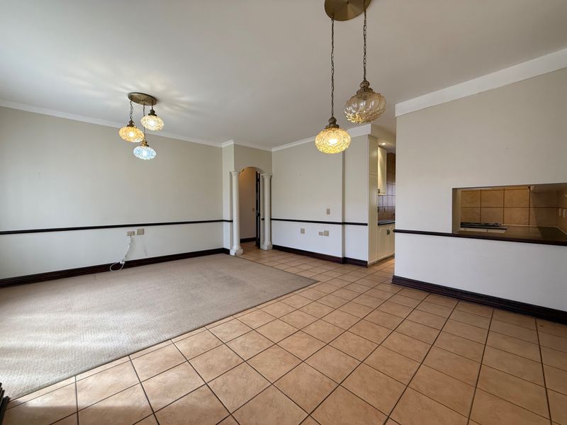 Spacious open-plan living and dining area featuring a mix of tiled and carpeted flooring, decorative lighting, and a convenient pass-through window to the kitchen.