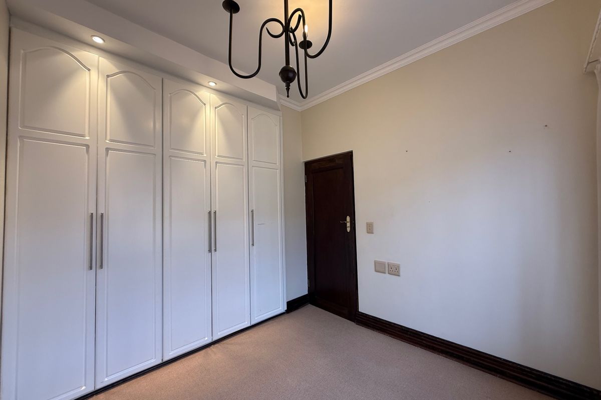 A clean, empty bedroom featuring ample built-in cupboard storage, recessed lighting, crown molding, and neutral carpeting.