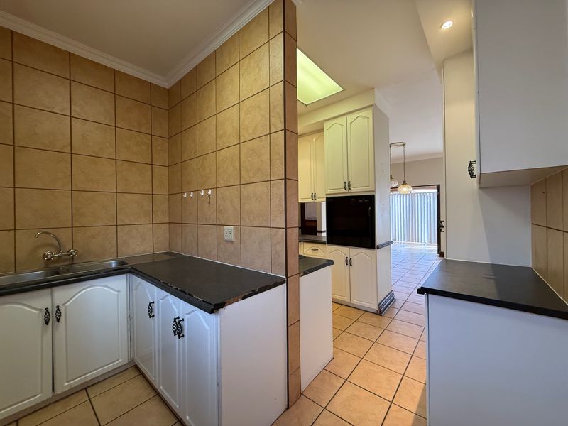 A functional kitchen featuring built-in cabinetry, laminate countertops, a stainless steel sink, and a built-in oven, with a tiled splashback and neutral floor tiles.