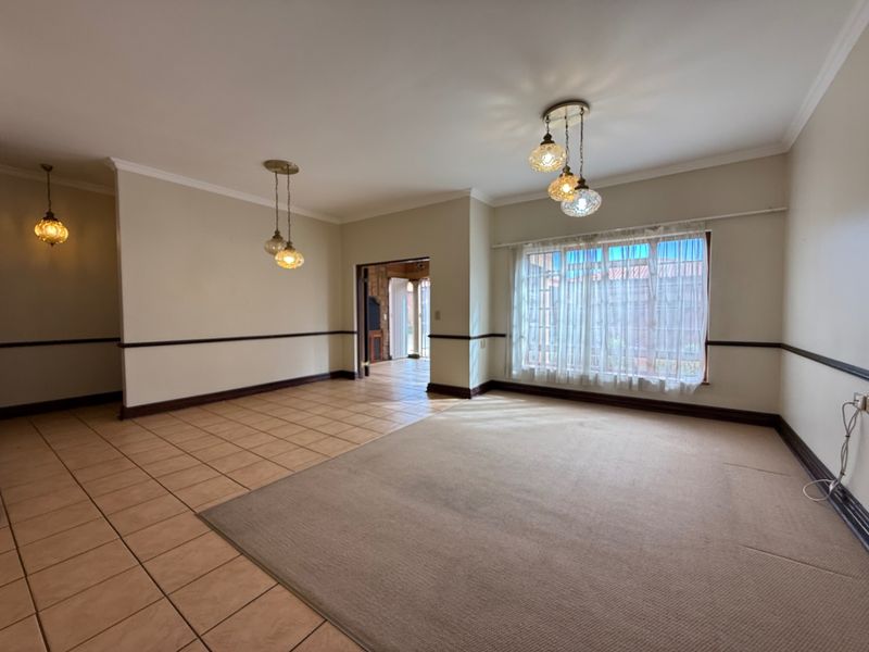 Spacious, empty living area featuring a combination of tiled and carpeted flooring, decorative pendant lighting, and a large window with natural light.