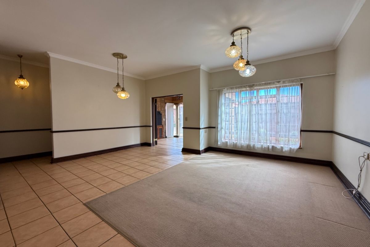 Spacious, empty living area featuring a combination of tiled and carpeted flooring, decorative pendant lighting, and a large window with natural light.