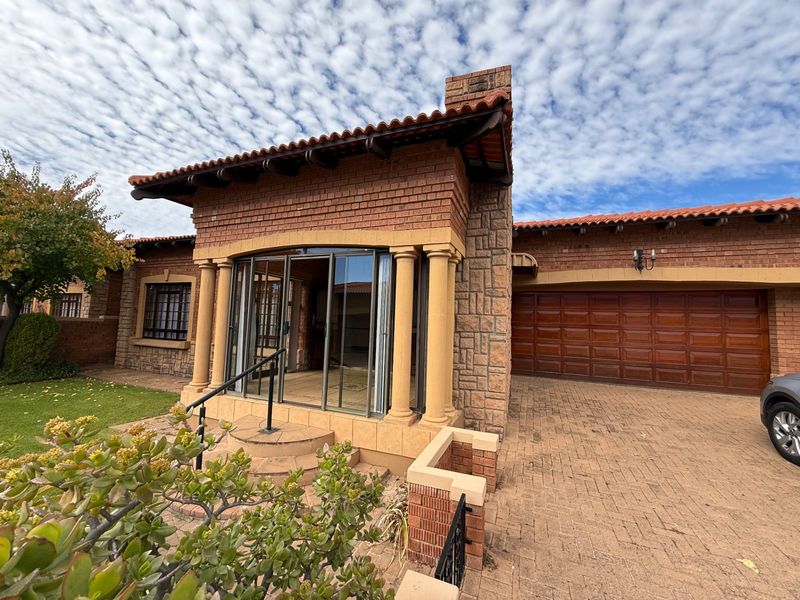 Front elevation of a brick townhouse featuring a double garage, paved driveway, and a covered entrance with decorative columns and sliding glass doors.