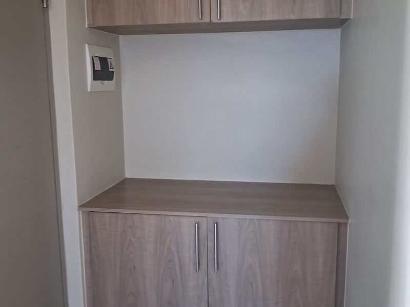 A compact scullery or utility area featuring modern wood-look built-in cabinetry with ample storage and a durable laminate countertop.