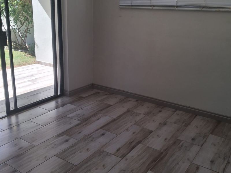 An empty living room featuring modern wood-look tile flooring, neutral walls, and a sliding glass door providing access to the outdoor patio area.