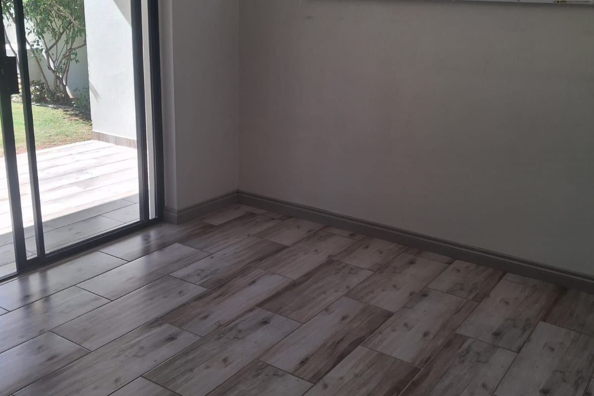 An empty living room featuring modern wood-look tile flooring, neutral walls, and a sliding glass door providing access to the outdoor patio area.