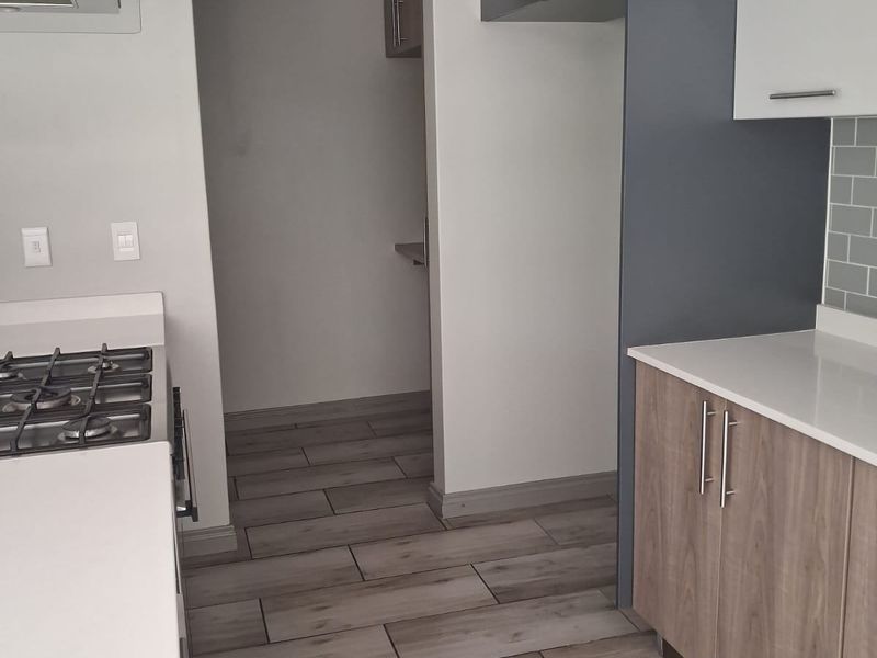 Modern kitchen featuring two-tone cabinetry, stone countertops, gas hob with extractor, and wood-look tiled flooring in a clean, contemporary finish.