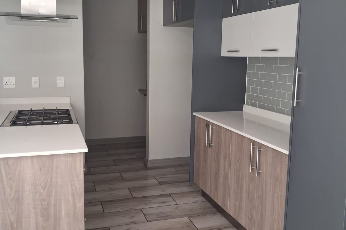 Modern kitchen featuring two-tone cabinetry, quartz countertops, gas hob with extractor fan, subway tile backsplash, and wood-look tiled flooring.