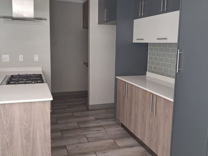 Modern kitchen featuring two-tone cabinetry, quartz countertops, gas hob with extractor fan, subway tile backsplash, and wood-look tiled flooring.