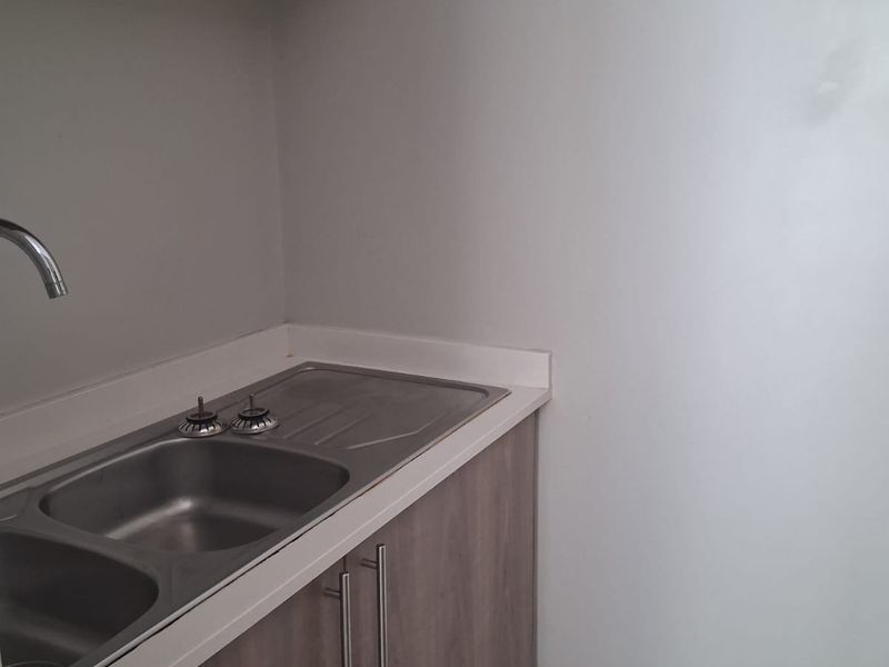 A compact scullery area featuring modern laminate cabinetry, a stainless steel double sink, and a clean countertop, providing functional prep and wash-up space.