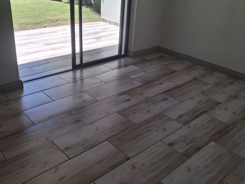 An empty living room featuring modern wood-look floor tiles and a large sliding glass door providing direct access to the rear patio and garden.