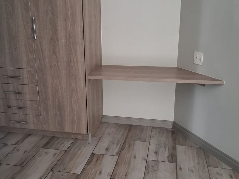 A clean bedroom corner featuring a modern built-in wardrobe with integrated desk space and wood-look tiled flooring.