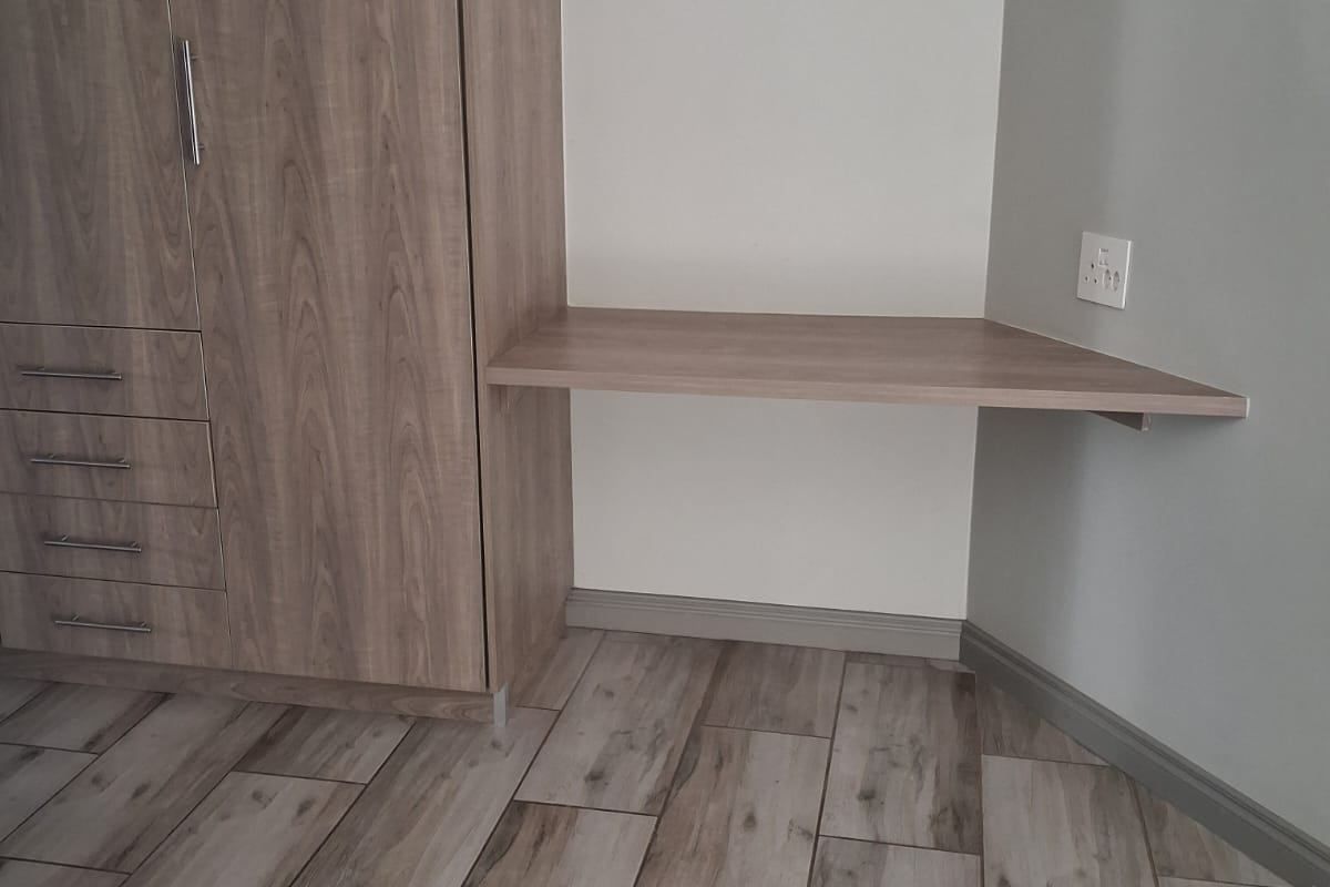 A clean bedroom corner featuring a modern built-in wardrobe with integrated desk space and wood-look tiled flooring.