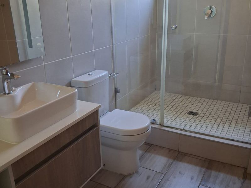 Modern bathroom featuring a wood-look vanity, vessel sink, toilet, and a glass-enclosed shower with tiled finishes.