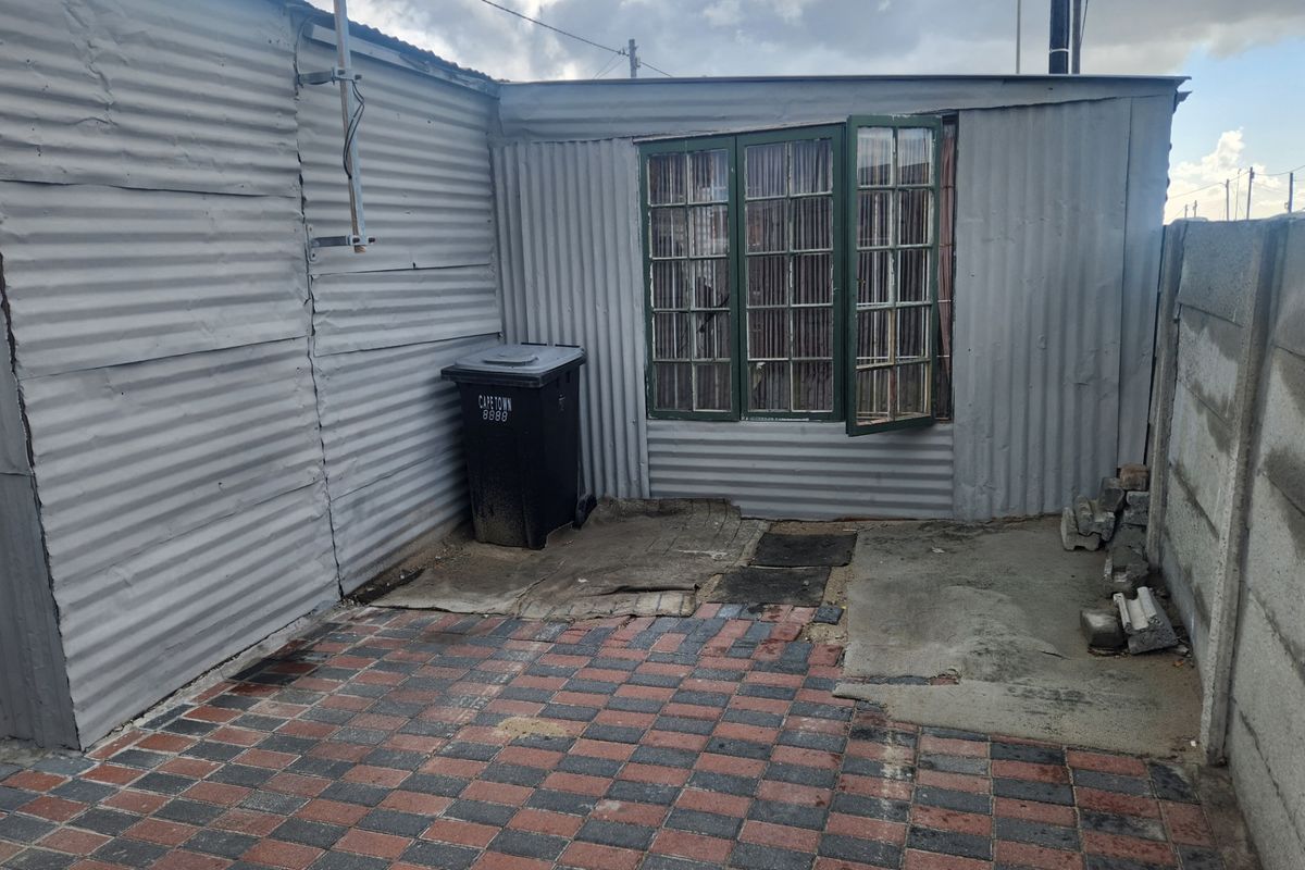 A rear exterior view showing a corrugated metal structure with a paved patio area and a precast concrete boundary wall.