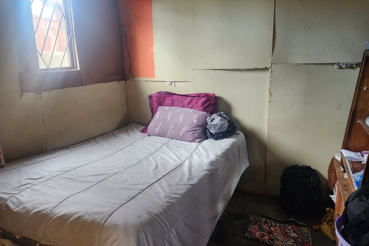 A small bedroom featuring basic wall paneling and a window with security bars, currently requiring significant cosmetic updates and repairs to wall finishes.