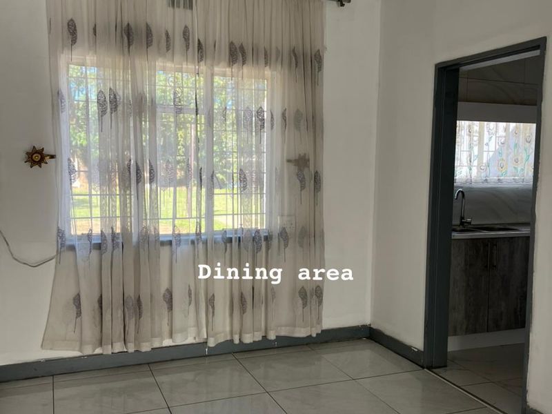 A bright, empty dining area featuring tiled flooring, security bars on the window, and direct access to the adjacent kitchen.