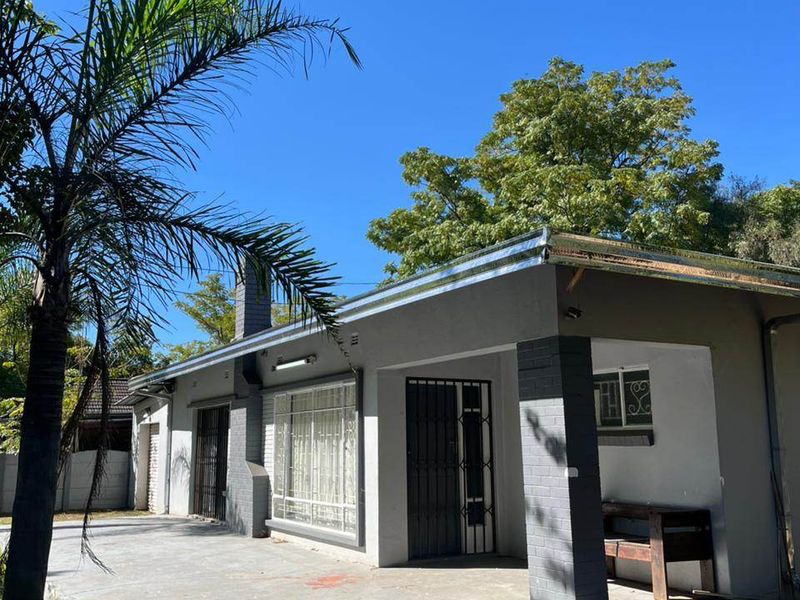 Rear view of the house featuring a covered patio area, brick chimney, and concrete paving under a clear blue sky.