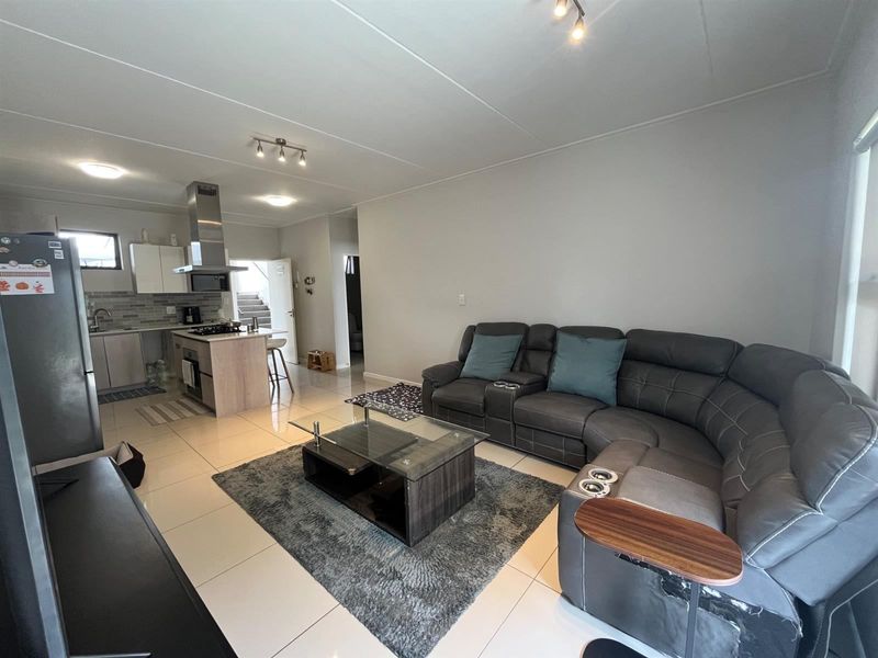 An open-plan living and kitchen area featuring modern tiled flooring, contemporary cabinetry, and a functional kitchen layout with integrated appliances.