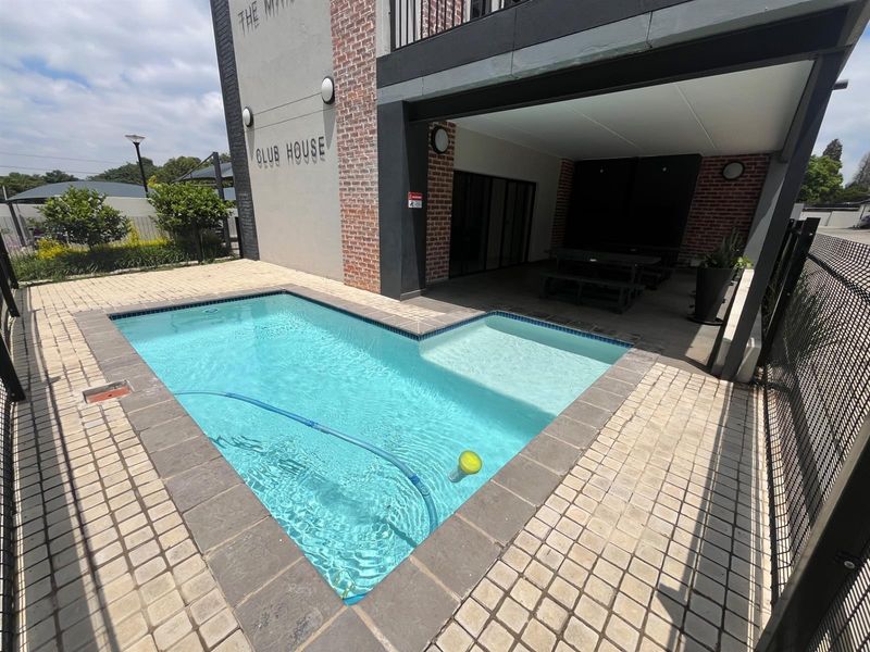 A well-maintained communal pool area featuring a paved deck, adjacent covered patio, and modern brick and plaster building facade.