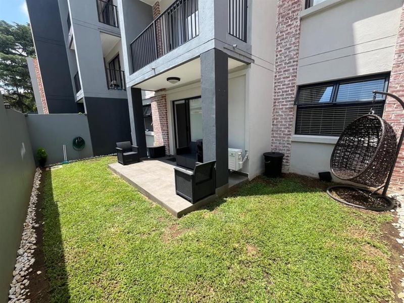 A private rear garden featuring a tiled patio area, well-maintained lawn, and direct access to the apartment via a sliding door.