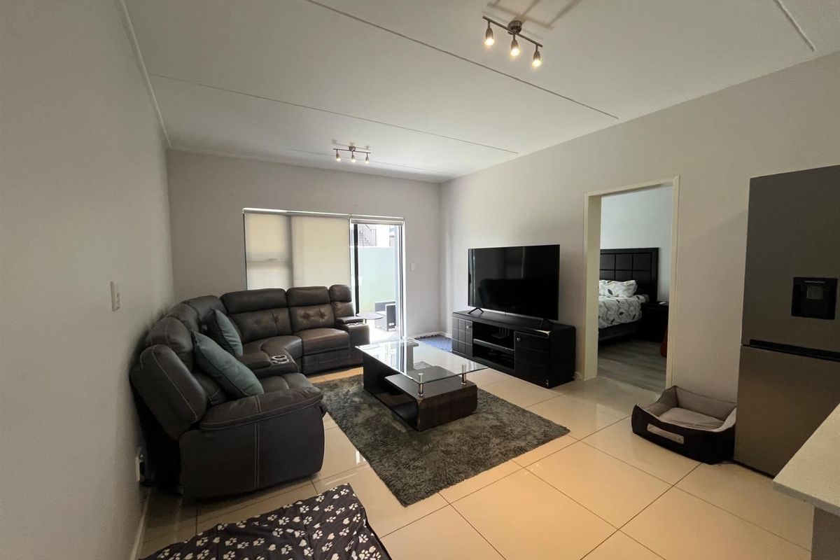 A well-maintained living room featuring neutral tiled flooring, modern track lighting, and a sliding glass door providing access to the outdoor area.