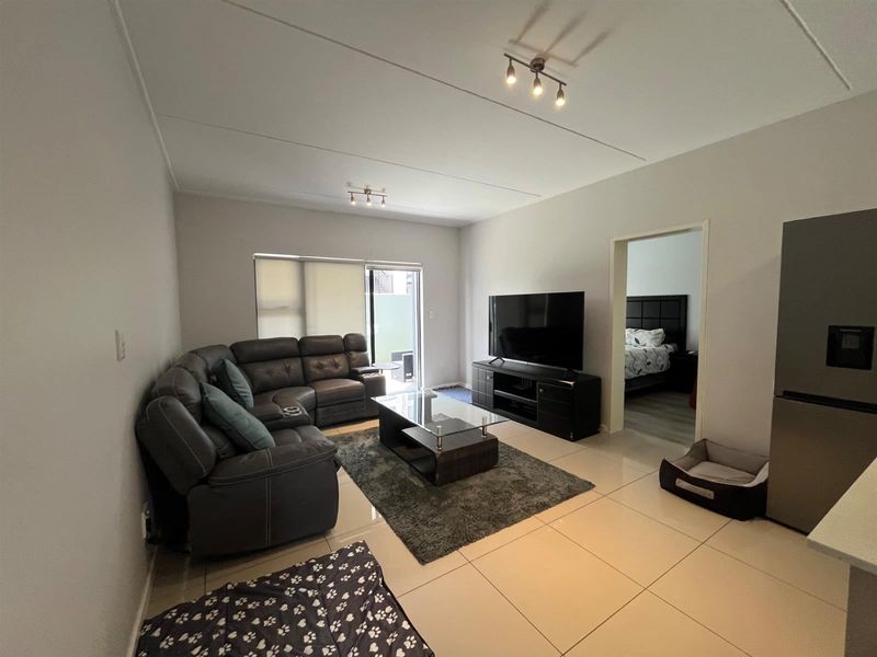 A well-maintained living room featuring neutral tiled flooring, modern track lighting, and a sliding glass door providing access to the outdoor area.