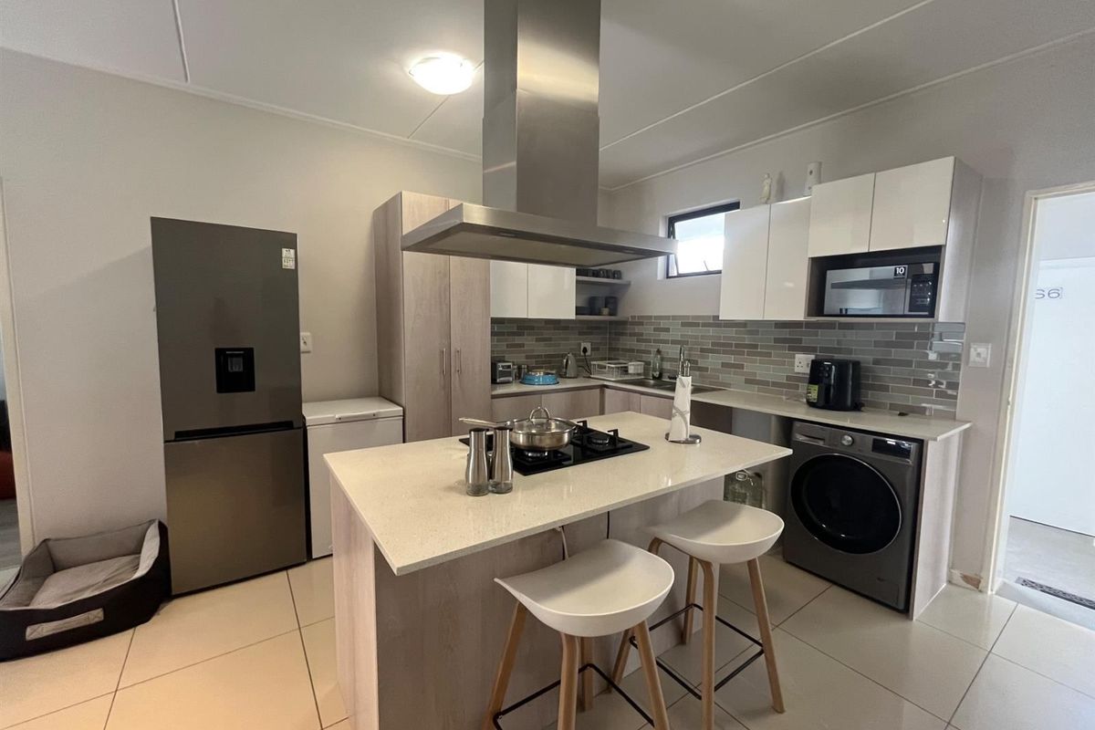Modern kitchen featuring a central island with gas hob, stainless steel extractor fan, quartz countertops, subway tile backsplash, and integrated laundry appliances.