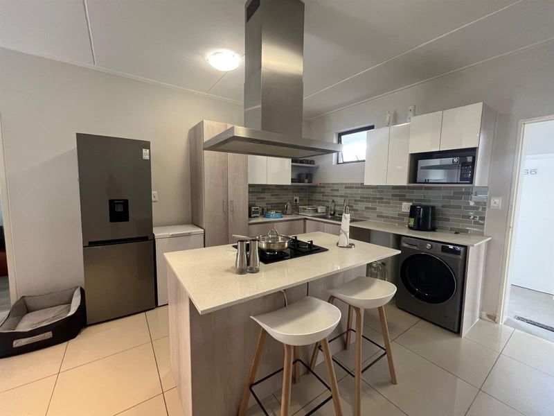 Modern kitchen featuring a central island with gas hob, stainless steel extractor fan, quartz countertops, subway tile backsplash, and integrated laundry appliances.