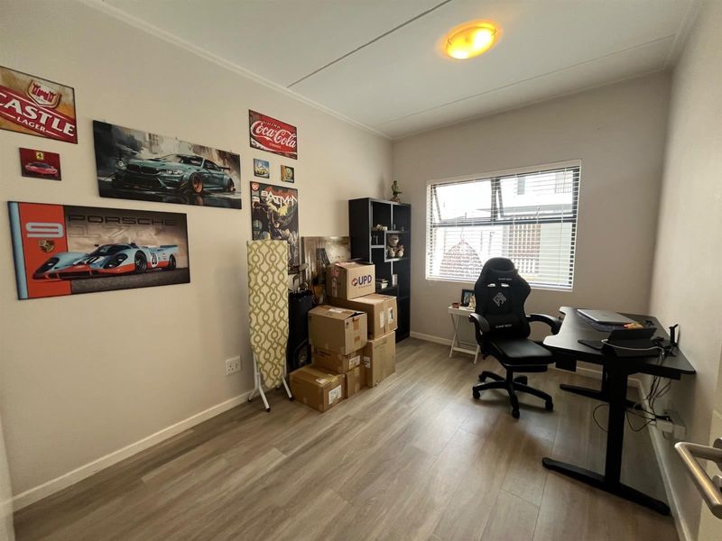 A functional bedroom or home office space featuring modern laminate flooring and a top-hung window providing natural light.