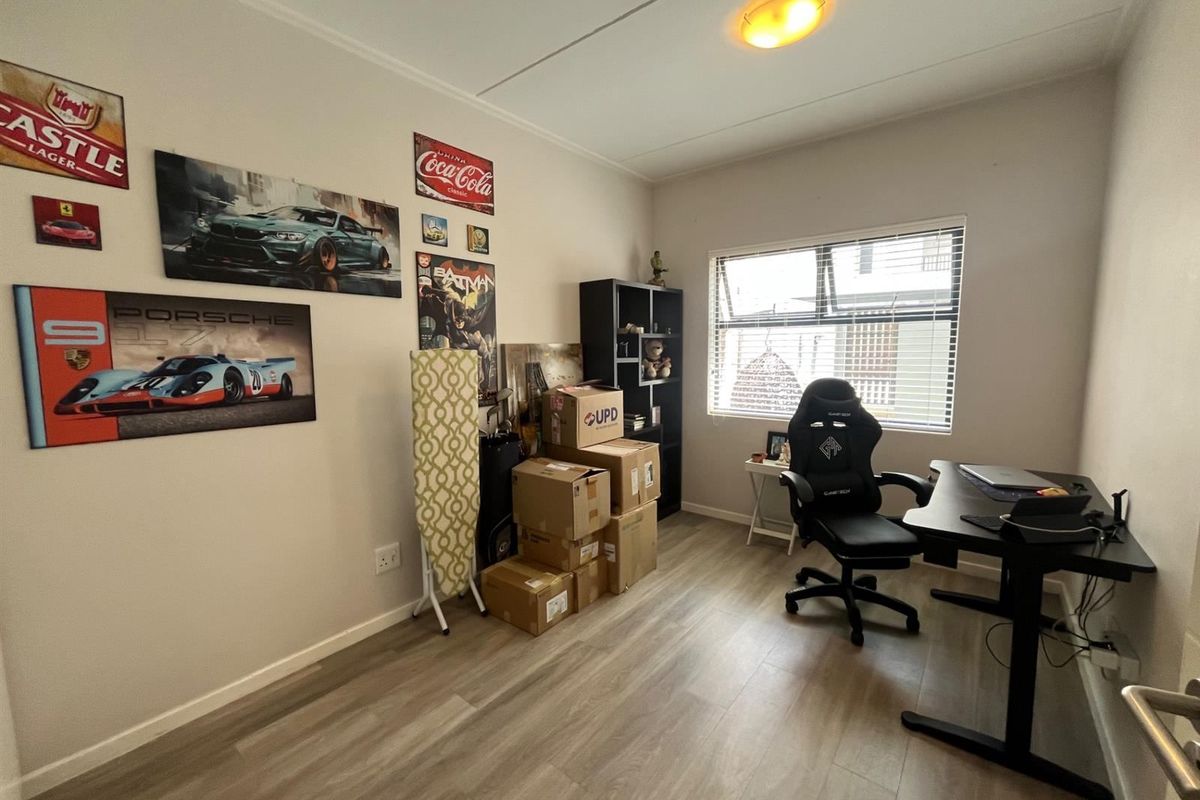 A functional bedroom or home office space featuring modern laminate flooring and a top-hung window providing natural light.