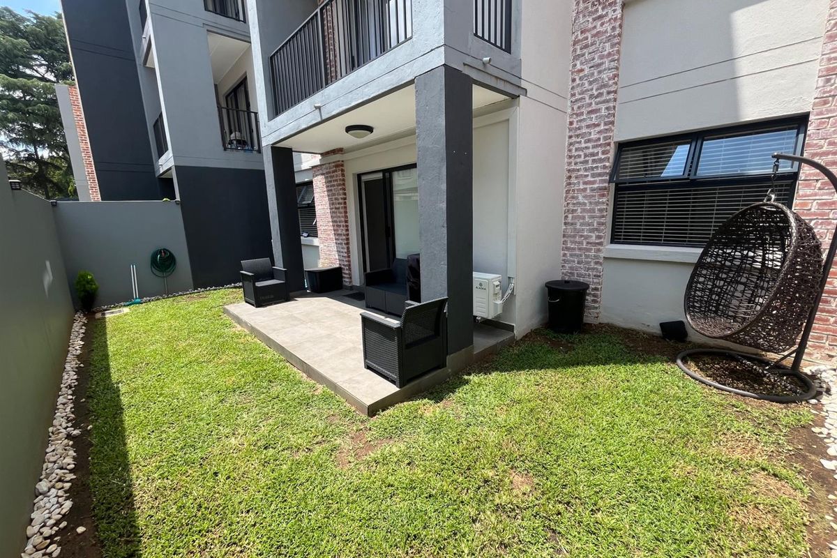 A private rear garden featuring a tiled patio area, brick-accented exterior walls, and a small lawn space accessible via sliding glass doors.