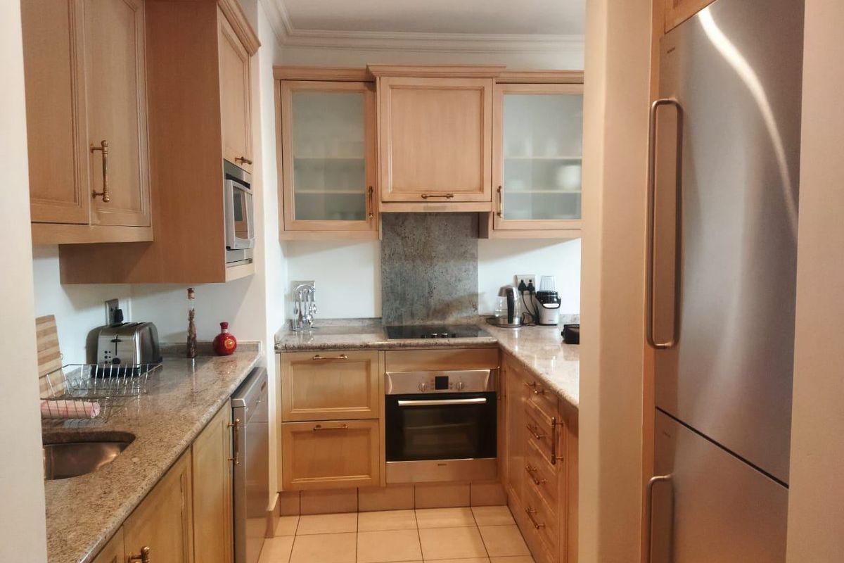 A functional kitchen featuring light wood cabinetry, granite countertops, a built-in oven, hob, and extractor fan with tiled flooring.