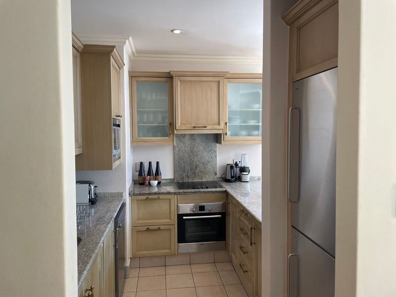 A functional kitchen featuring light wood cabinetry, granite countertops, a stone splashback, and integrated appliances, finished with tiled flooring and crown molding.