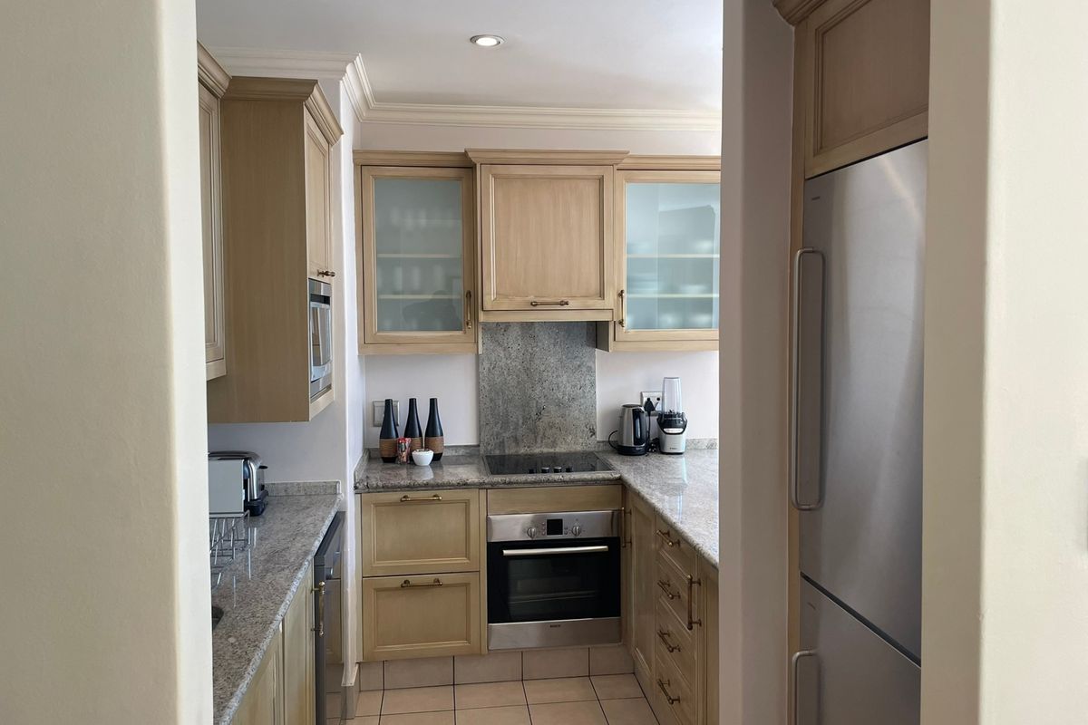 A functional kitchen featuring light wood cabinetry, granite countertops, a stone splashback, and integrated appliances, finished with tiled flooring and crown molding.