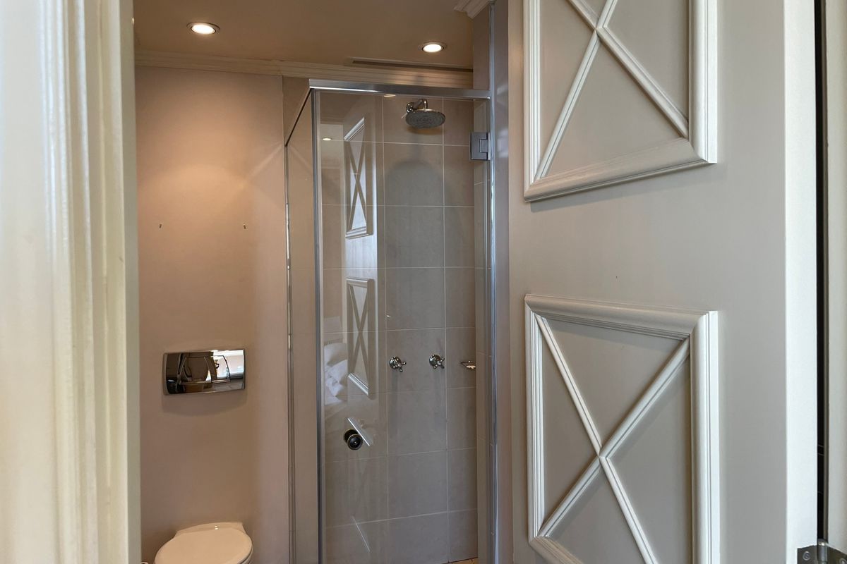 A clean and modern bathroom featuring a glass-enclosed shower, wall-mounted toilet, and elegant panelled door detailing.