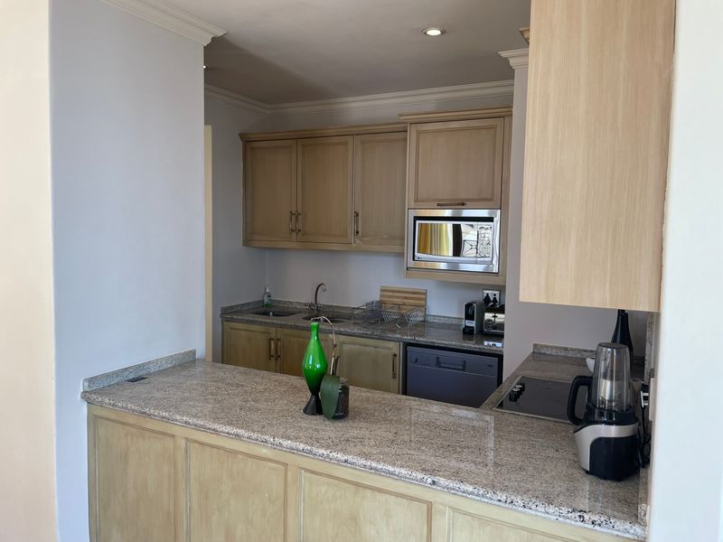 A functional kitchen featuring granite countertops, built-in wooden cabinetry, an integrated microwave, and a built-in hob with a breakfast bar area.