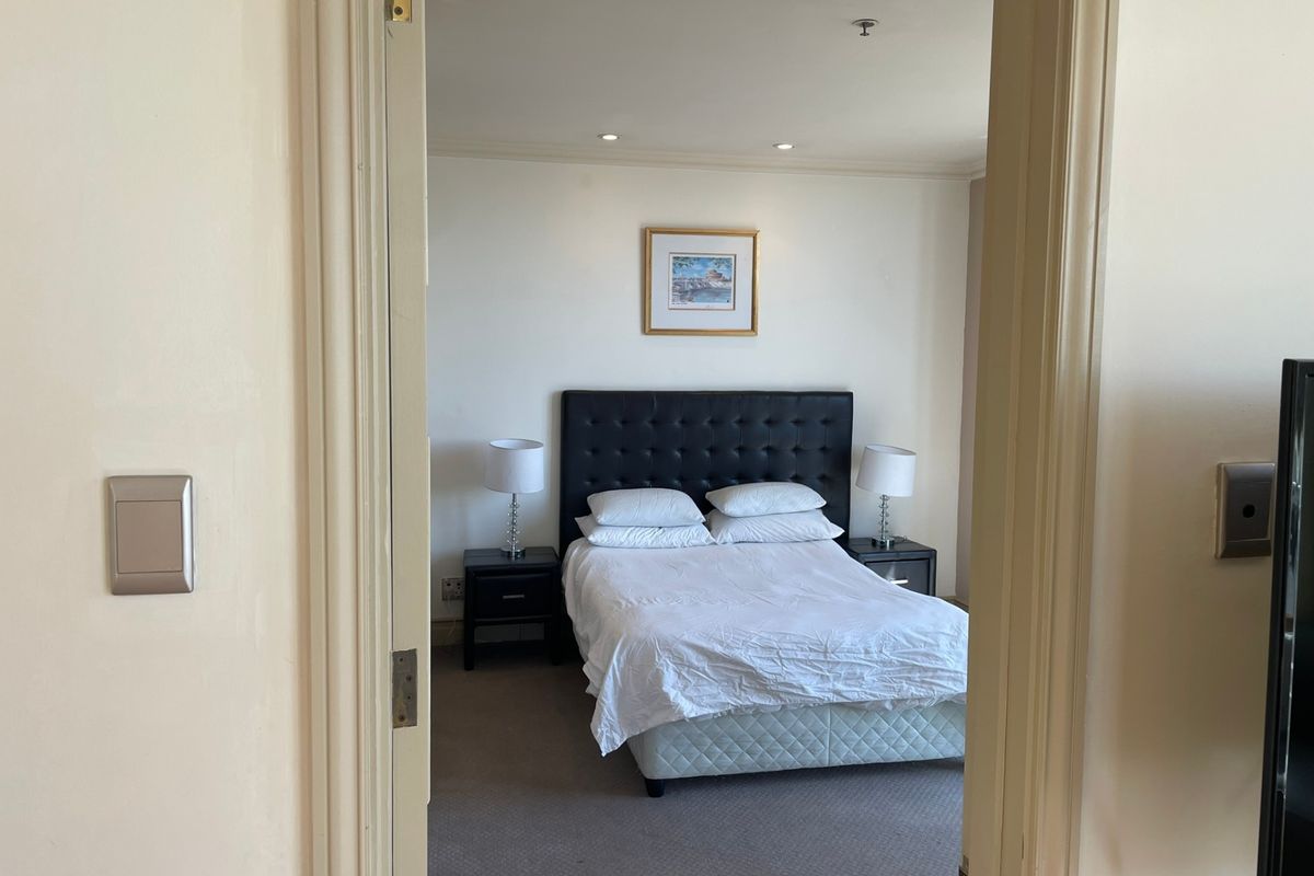 A well-lit bedroom featuring neutral carpeting and recessed ceiling lighting, viewed through a doorway.