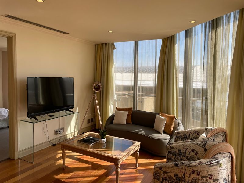 A bright living room featuring hardwood flooring, recessed lighting, and expansive floor-to-ceiling windows that provide ample natural light.