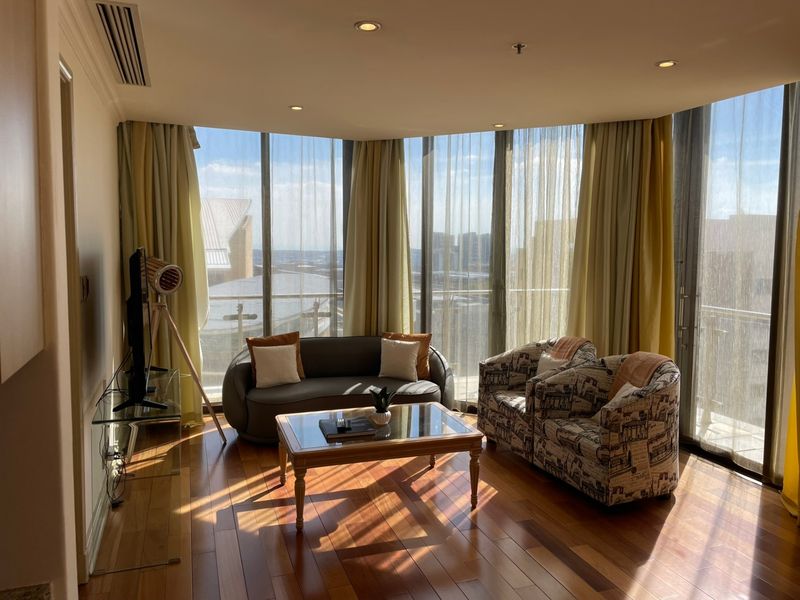 Bright living room featuring polished hardwood flooring, expansive floor-to-ceiling windows with natural light, and integrated recessed lighting.