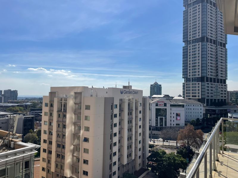 An elevated urban view from a balcony overlooking surrounding high-rise buildings and city infrastructure.