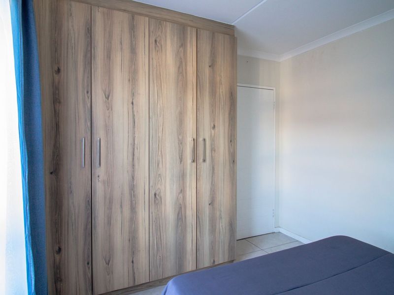 A well-maintained bedroom featuring modern wood-grain built-in cupboards and neutral tiled flooring.