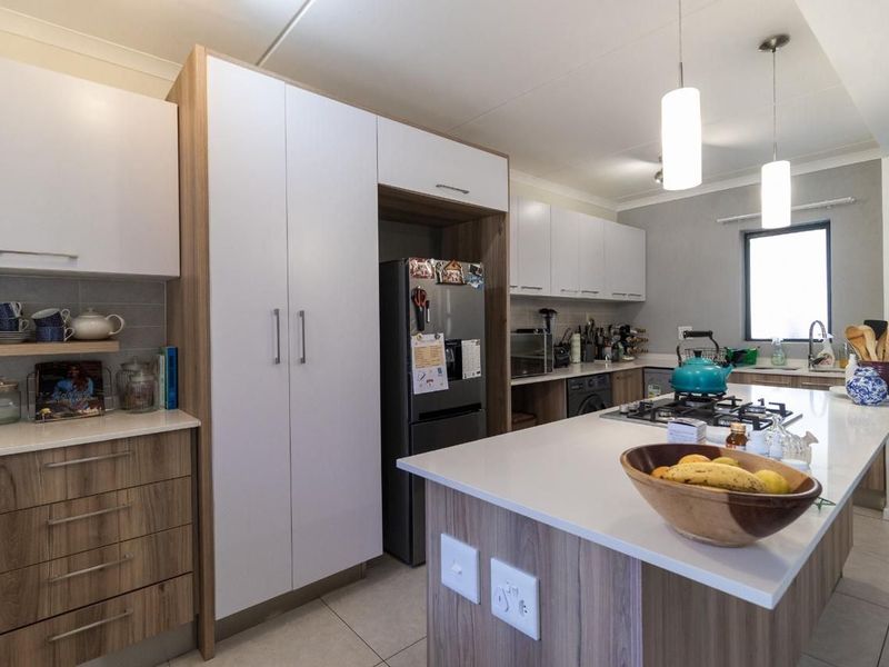 Modern kitchen featuring a central island with a gas hob, ample built-in cabinetry, stone countertops, and contemporary pendant lighting.